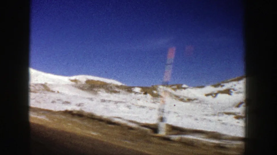 A moving-vehicle view in Aspen, Colorado, with snow on the slope and a red-and-white roadside marker under a deep blue sky.