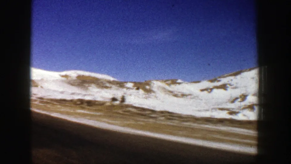 1961 passenger-view footage near Aspen showing a road running past snow-covered slopes beneath a clear blue sky.