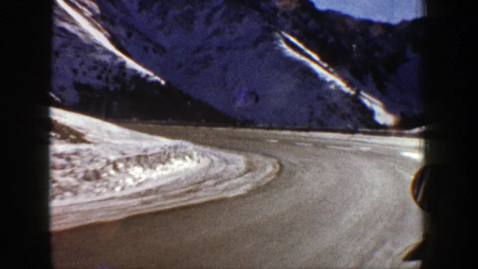 Aspen-area mountain road curves through snowbanks and steep dark slopes, filmed from inside or beside a moving vehicle in 1961.