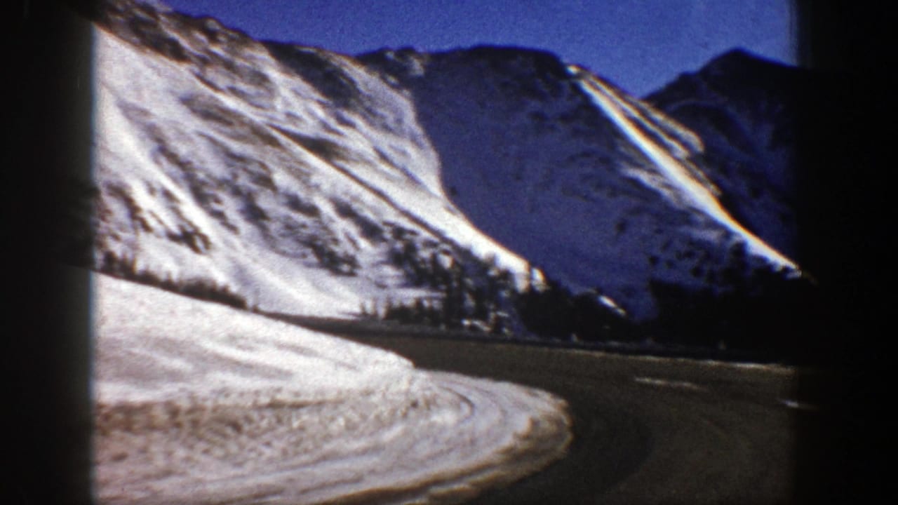 Roadside snowbank and steep snowy mountain slope seen from a moving vehicle.