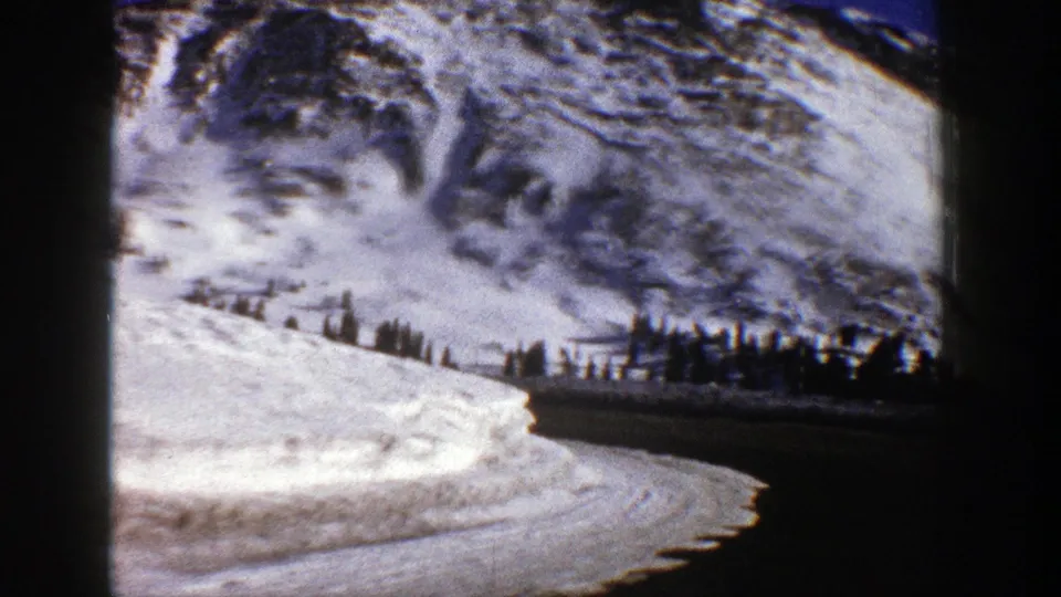Aspen, Colorado winter roadway view with snowbanks, a dark curve of pavement, evergreens, and rugged alpine slopes.