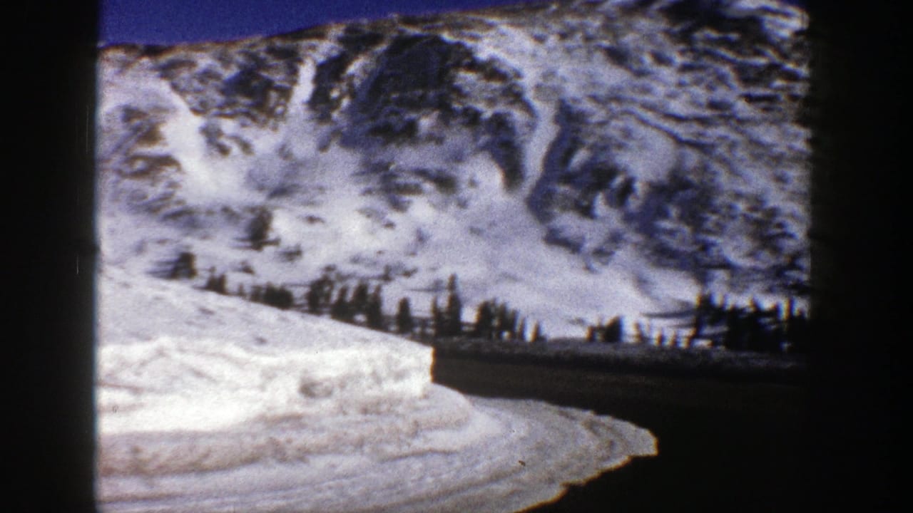 Snowy mountain road curving beside high snowbanks and dark evergreen trees.