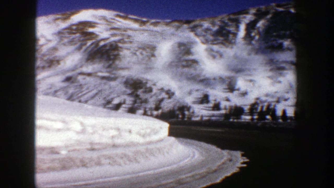 Curving snow-lined road beneath bright mountain slopes and a clear blue sky.