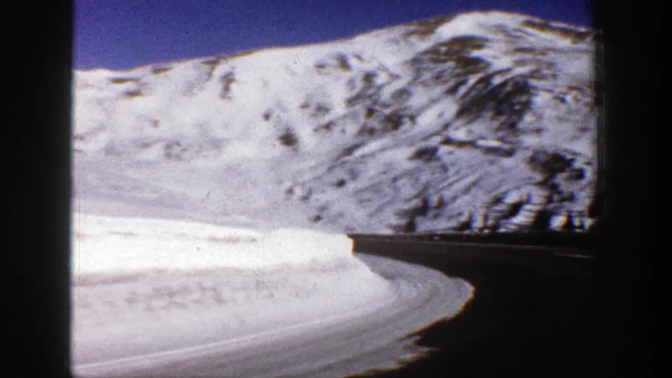 1961 8mm winter travel frame showing a dark road at the base of broad snow-covered Aspen mountain slopes.