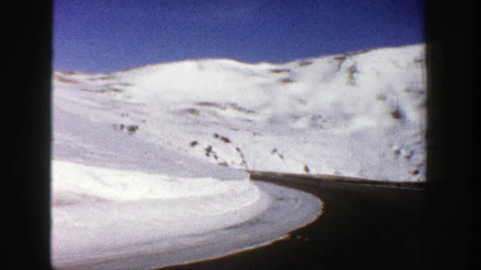 Late clip frame from 1961 Aspen footage showing a rounded snowbank, dark mountain road, and open white slope.