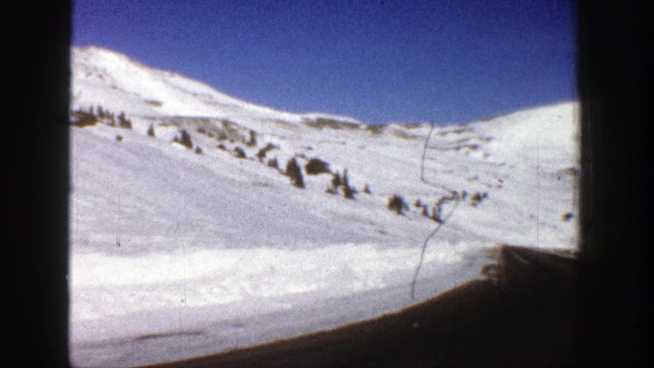 Snowy mountain ridge and winding road partly framed by dark vertical vehicle edges.