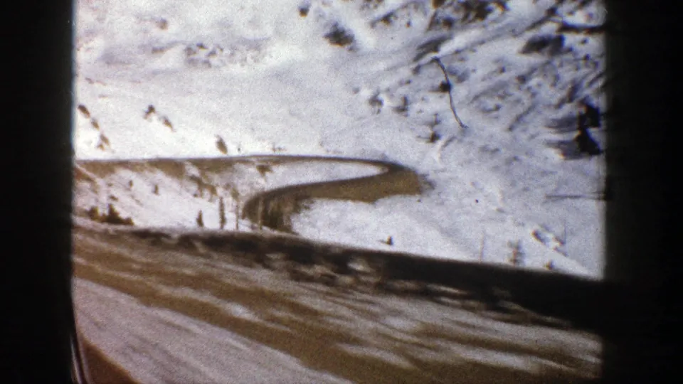 A snowy Aspen slope and curved dirt or mountain road pass by from a vehicle viewpoint in this 1961 8mm home-movie frame.