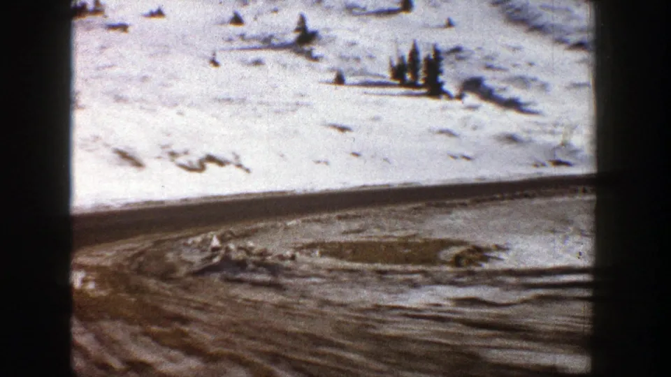 1961 Aspen winter road scene with tire tracks, snowfields, scattered evergreens, and visible 8mm frame edges.