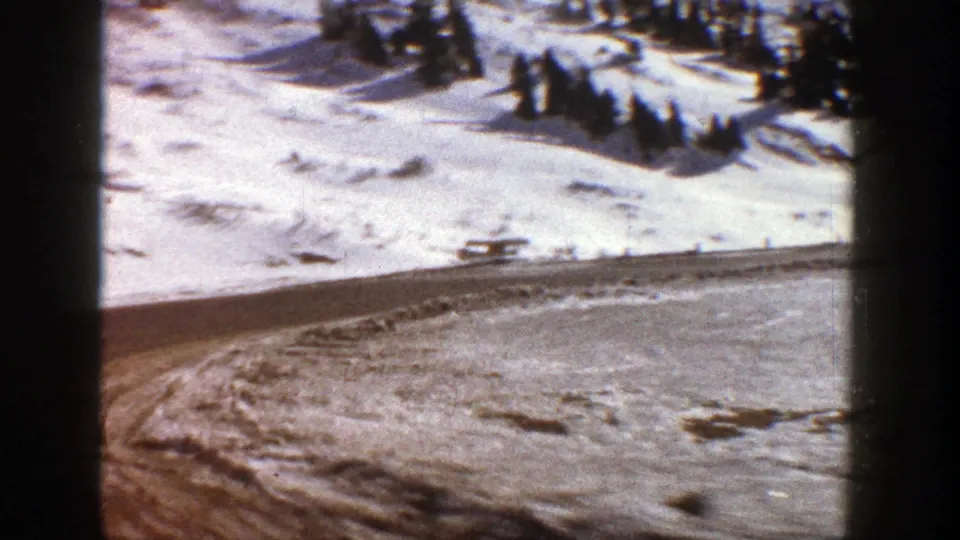 1961 Aspen winter road view with snowy banks, a small distant vehicle-like form, evergreens, and contact-sheet borders.