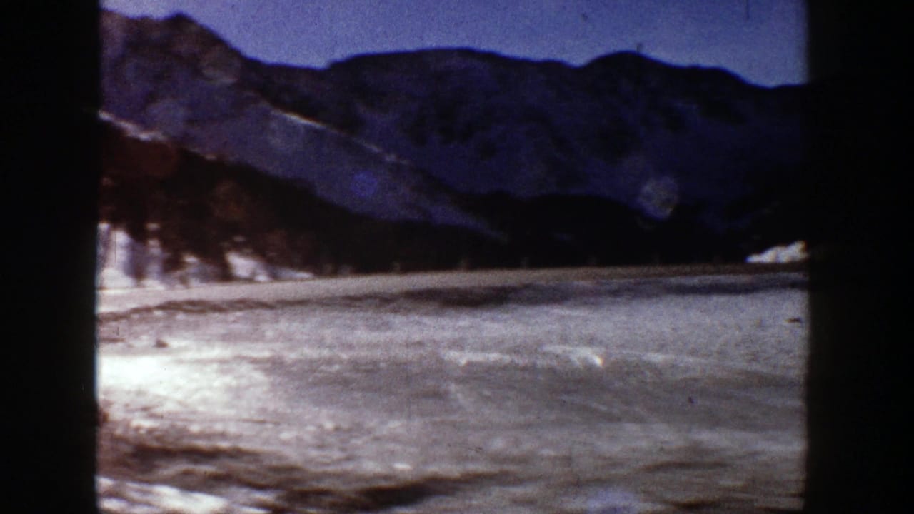 Snowy open area and dark mountain ridge viewed from a moving vehicle.