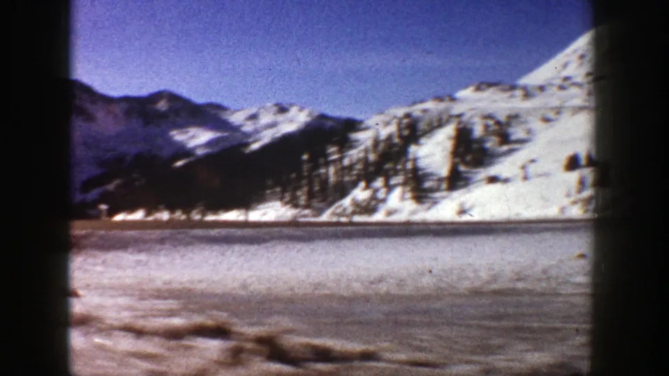 1961 8mm mountain travel frame with icy foreground, snow-covered hills, conifer clusters, and distant Colorado peaks.