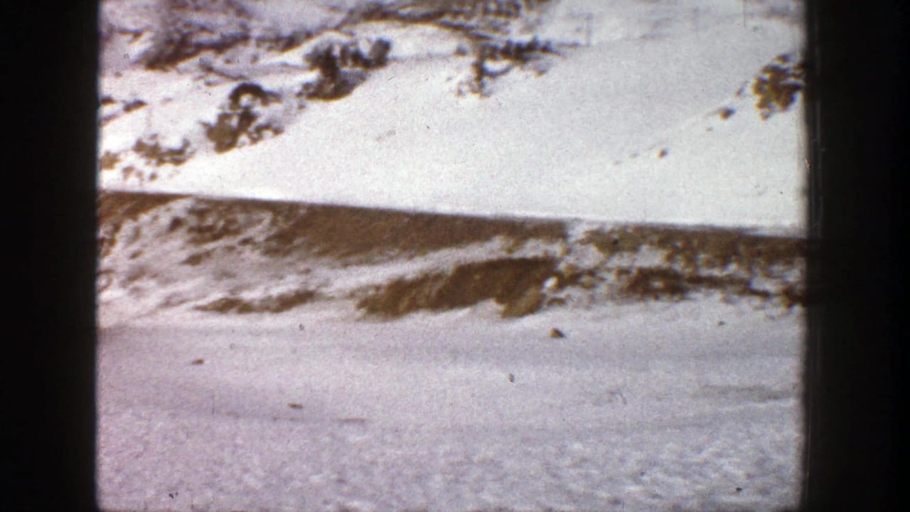 Snowy hillside with scattered dark rocks and trees above a flat winter foreground.