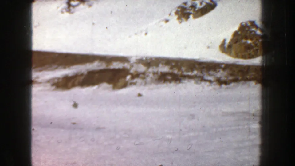 Aspen, Colorado 1961 8mm frame showing a broad snowfield beneath a rocky, tree-dotted mountain slope.