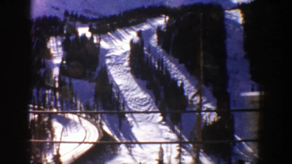 1961 8mm view of snow-covered Aspen slopes with winding runs, dark trees, and visible film-frame borders.