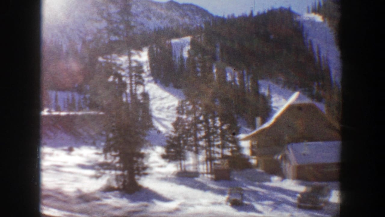 1961 Aspen, Colorado home-movie frame showing rustic cabins, snowfields, evergreens and mountain ridges in soft 8mm color.