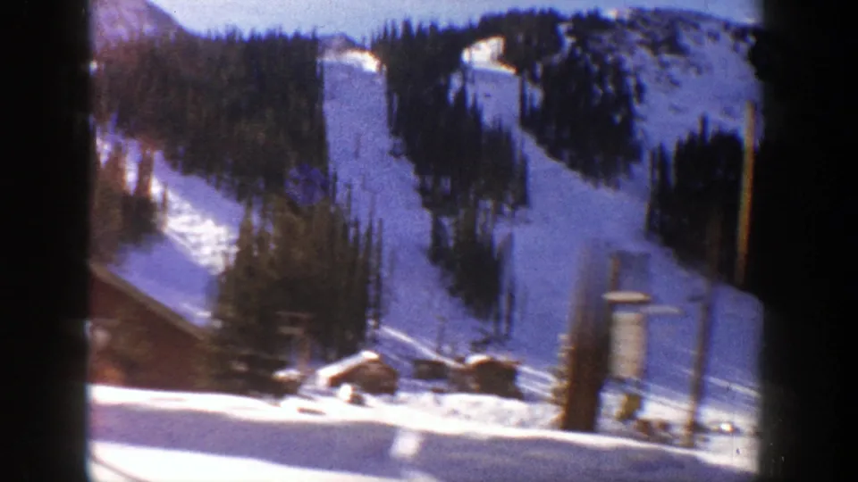 Aspen, Colorado winter home-movie view showing a snow-covered slope, nearby buildings, parked cars and utility poles in 1961.