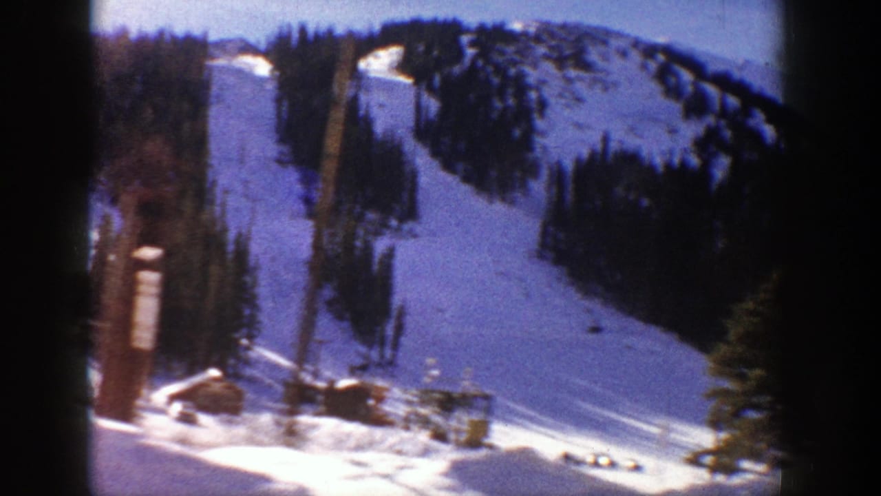 1961 Aspen, Colorado home-movie frame showing a sunlit snowy slope, evergreen trees, and ski-area infrastructure near the base.