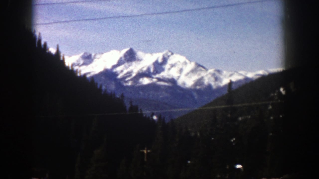Distant snowy peaks framed by dark forested hills and faint overhead wires.