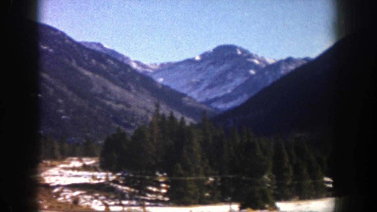 Snowy valley landscape with evergreen trees and mountains seen from inside a vehicle.