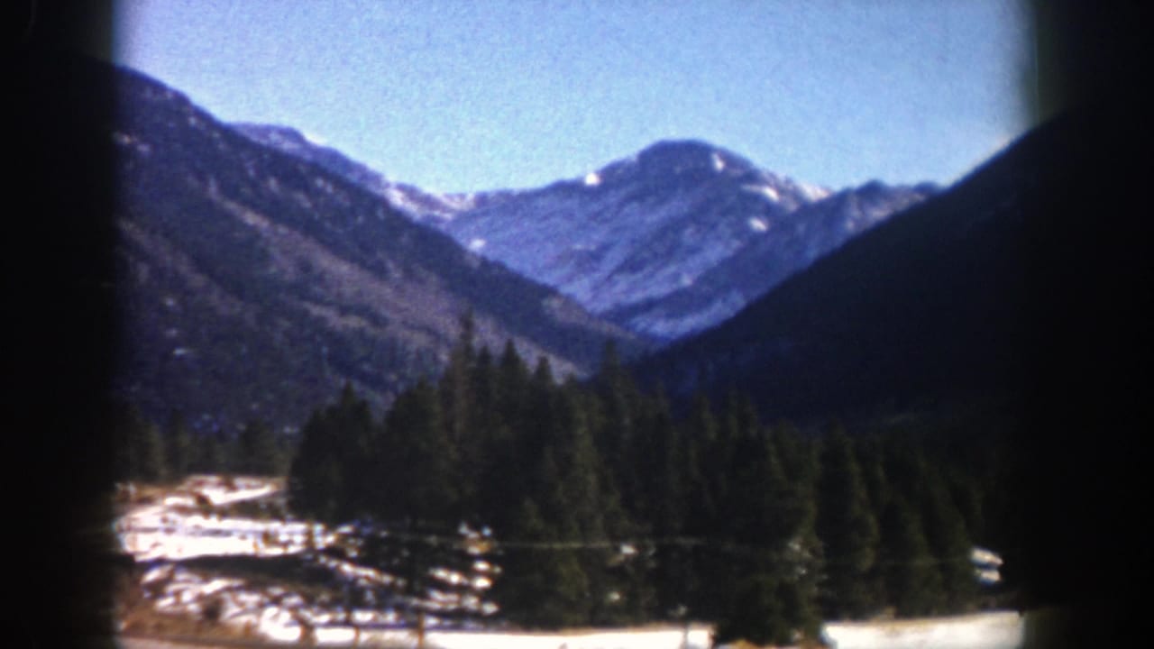 1961 Aspen, Colorado 8mm frame showing snow-dusted mountains, evergreen trees, and a bright blue sky from a moving viewpoint.