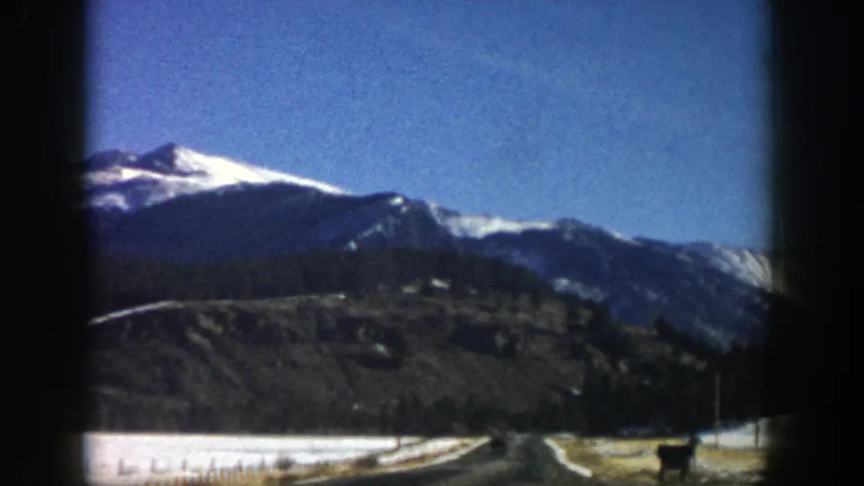 1961 Aspen, Colorado 8mm frame showing a curving road, snowy roadside, wooded slope, and snow-bright mountain ridge.