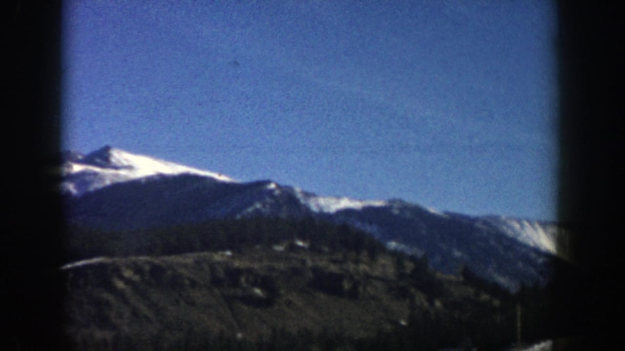 1961 Aspen, Colorado 8mm frame showing a snow-covered mountain ridge under blue sky with dark frame edges.