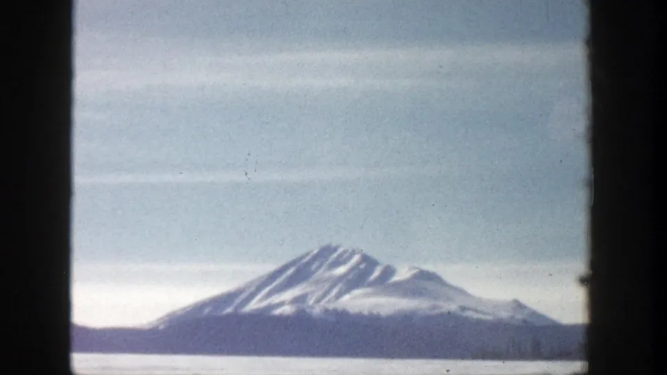1961 Aspen, Colorado 8mm frame with a distant snow-striped mountain beyond a pale lake or valley under hazy sky.
