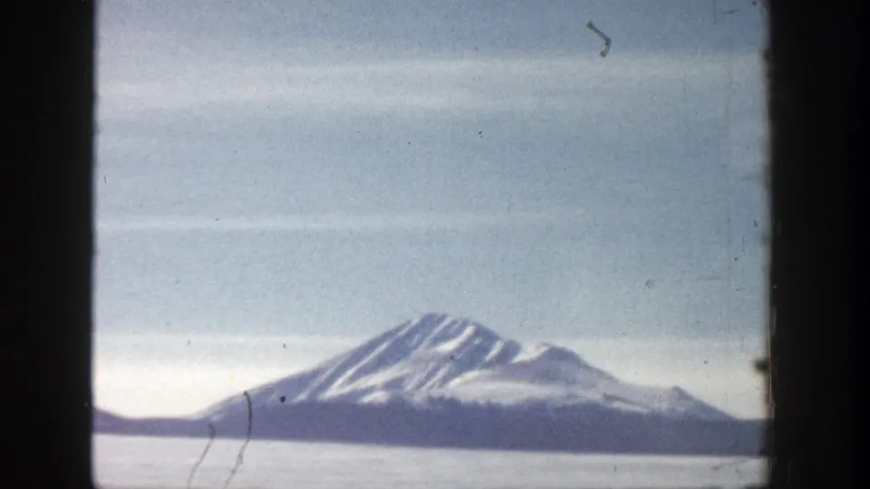 1961 Aspen, Colorado 8mm frame showing a distant snowy mountain across a pale lake or valley, with visible grain and haze.
