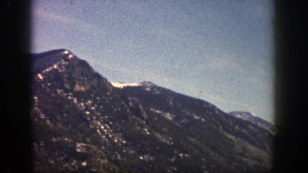 Dark mountain ridge under a pale blue sky with film frame borders.