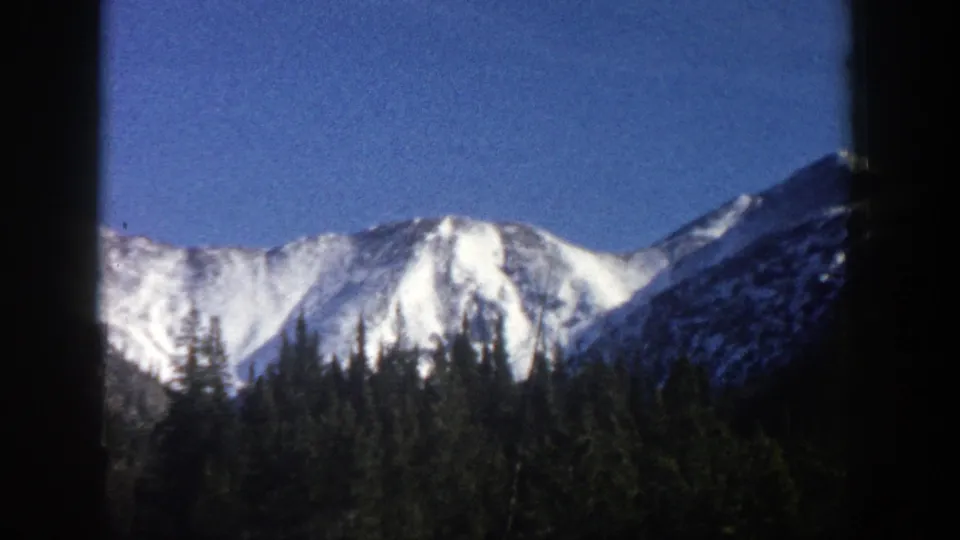 Aspen, Colorado 8mm home-movie frame with snow-bright peaks, dark forest, blue sky, and visible film edge shadows.