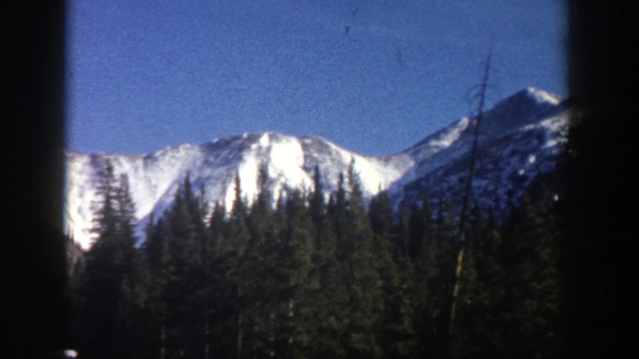 Snowy ridgeline and evergreen slopes under blue sky, partly obscured by a dark center frame edge.