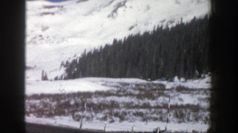 1961 Aspen, Colorado travel footage shows a snowy hillside, conifer stand, and valley floor from a moving home-movie viewpoint.