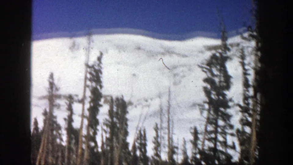 1961 Aspen winter scenery with snow-covered slopes framed by tall evergreen trees and 8mm film borders.