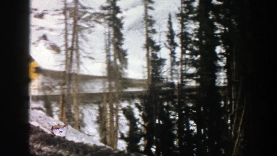 A snowy Aspen roadside scene with evergreens and a partially visible yellow warning sign in soft 8mm focus.
