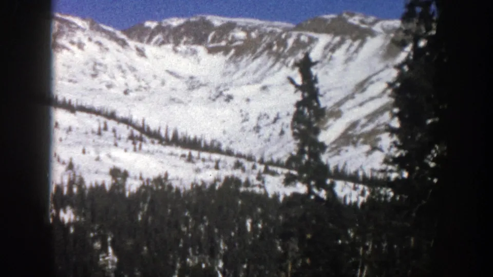 Wide 1961 Aspen mountain view showing a snowy basin, ridgelines, evergreens, and blue sky on 8mm film.