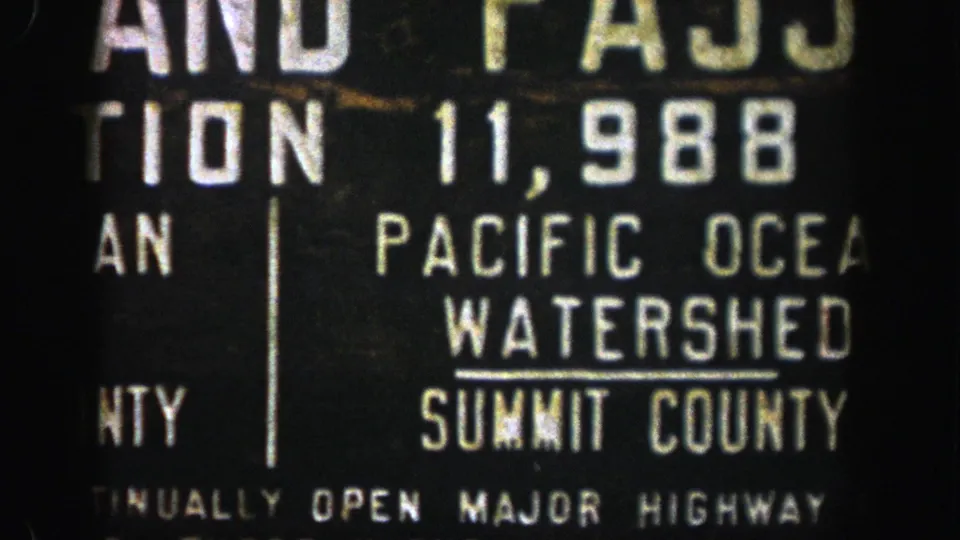 1961 Colorado home-movie frame with Pacific Ocean Watershed and Summit County lettering on a roadside sign.