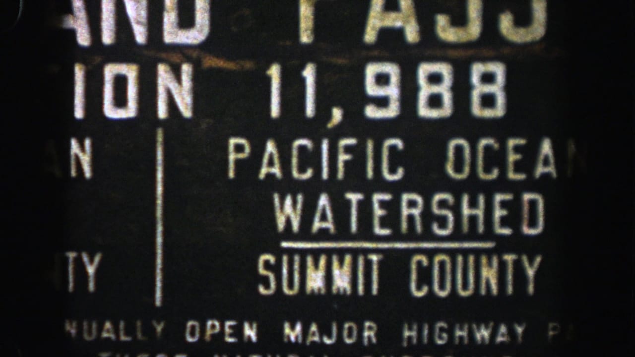 1961 Aspen-area 8mm frame of a dark highway sign cropped around Pacific Ocean Watershed and Summit County text.