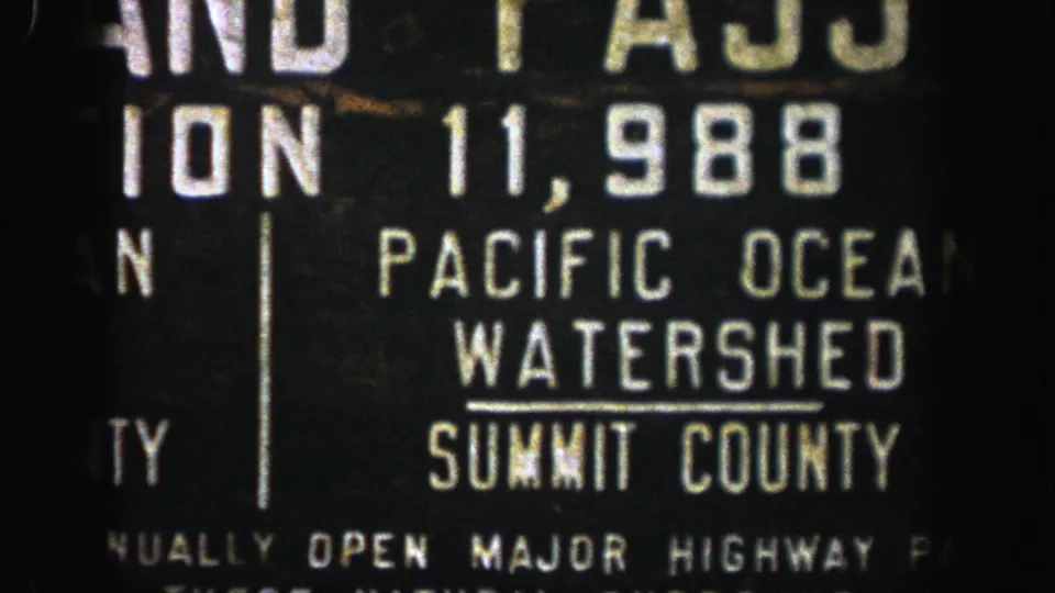 1961 Aspen-area 8mm frame of a dark highway sign cropped around Pacific Ocean Watershed and Summit County text.