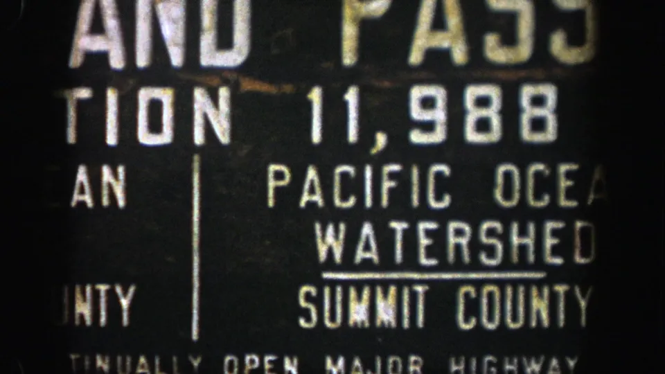 Cropped 1961 Colorado 8mm view of a roadside sign naming Pacific Ocean Watershed and Summit County.