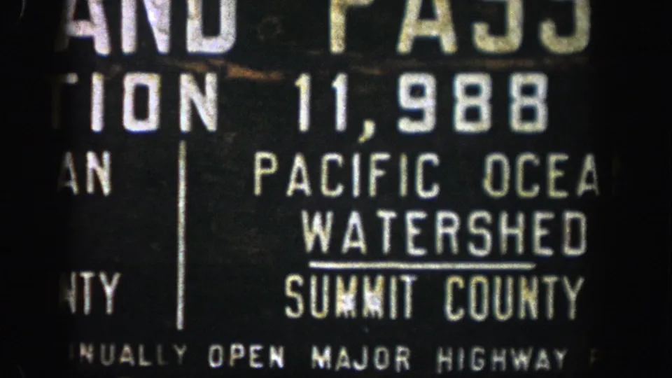 1961 Colorado 8mm frame showing a cropped roadside Pacific Ocean Watershed sign with Summit County lettering.