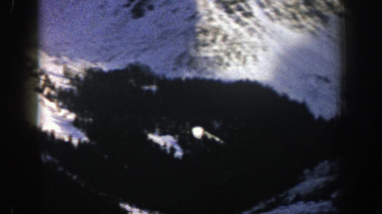 Dark tree-covered hillside below bright snow and sunlit mountain terrain.