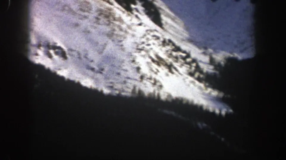Handheld 8mm view of an Aspen winter mountainside with sunlit snow, scattered evergreens, and deep shadows.