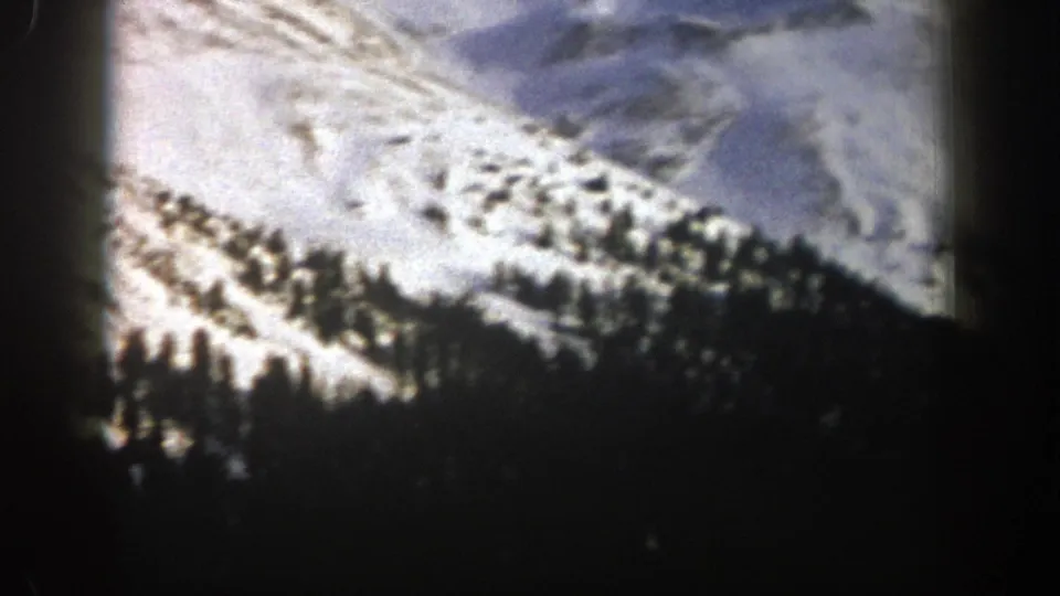 1961 Aspen 8mm frame of a snow-covered mountain basin bordered by dense dark evergreen trees.