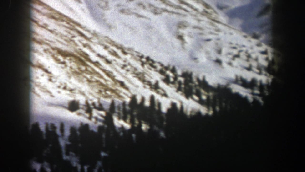 1961 Aspen, Colorado 8mm frame showing snowy mountain terrain with evergreen clusters and exposed ridgelines.