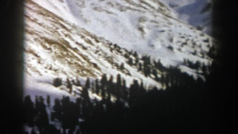 1961 Aspen, Colorado 8mm frame showing snowy mountain terrain with evergreen clusters and exposed ridgelines.