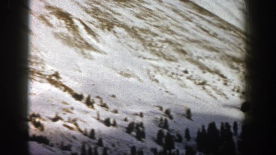 1961 Aspen, Colorado 8mm frame of a snow-covered hillside with sparse evergreens and exposed winter ground.