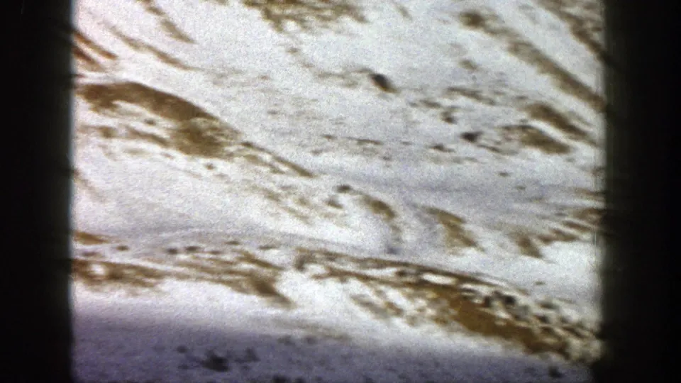 1961 Aspen, Colorado 8mm frame showing a broad snowy slope, exposed ridges, and darker terrain near the lower edge.