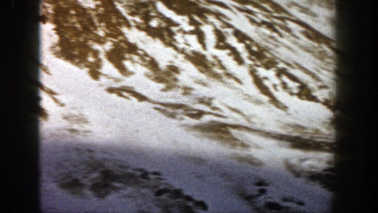 Snow-covered mountain slope with exposed rocky patches and dark film borders.