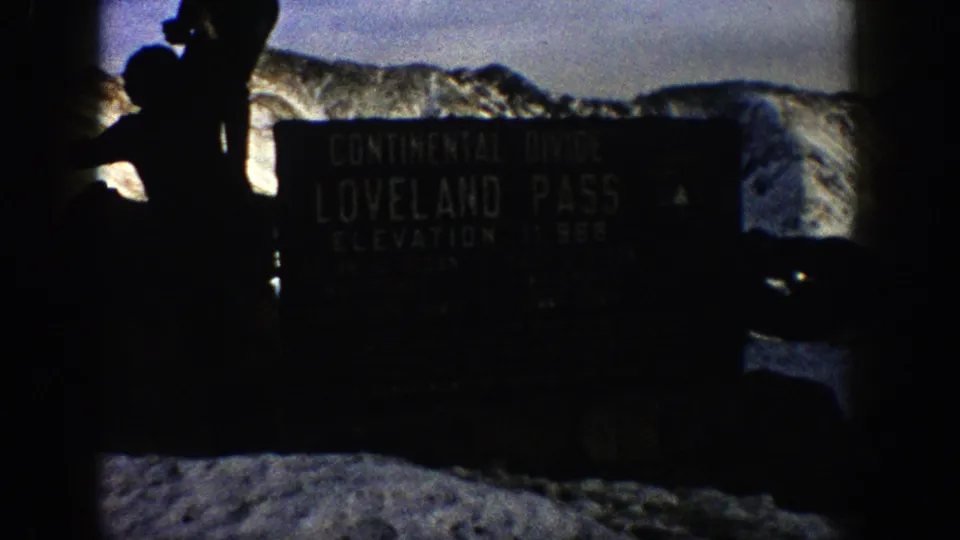Silhouetted visitor stands near the Loveland Pass Continental Divide sign in a snowy 1961 Colorado mountain scene.