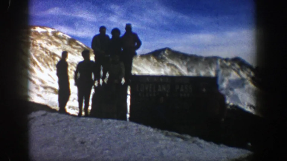 End frame of the 1961 Loveland Pass scene, with silhouetted travelers, a dark Continental Divide sign, and snowy Colorado mountains.